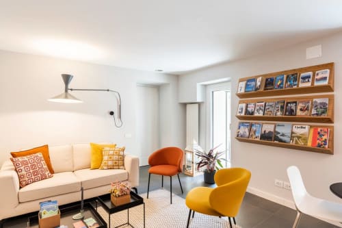 Moderna sala soggiorno con divano color crema, poltrone gialle e arancioni, scaffali in legno e vista sulla città a Camere d'Aria B&B