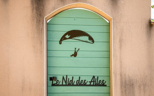 Green wooden door with parasailing illustration, entrance to Le Nid des Ailes villa room in Millau