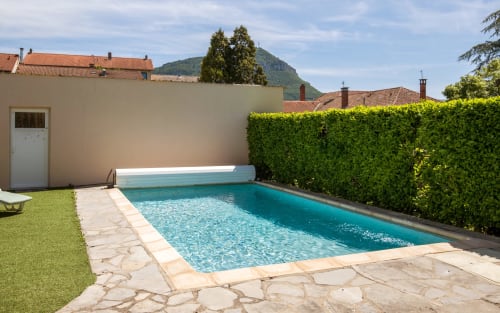 Private pool with turquoise water, lounge chairs, and green hedge at villa in Millau, France