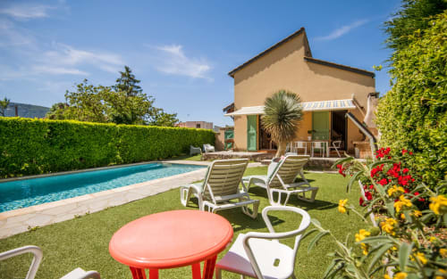 Sunny backyard villa in Millau with private pool, lounge chairs, flowering garden, and terracotta house