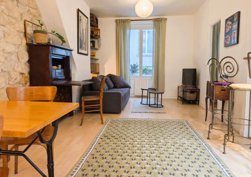 Spacious Parisian apartment living room with wooden dining table, dark sofa, fireplace, and balcony doors overlooking Paris