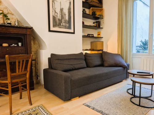 Modern Paris apartment living room with dark gray sofa, wooden chair, shelving, and city views at Conciergerie Saint Martin