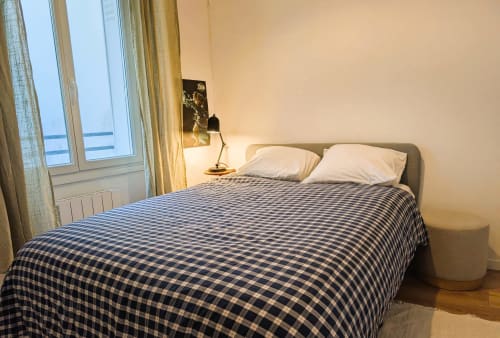 Modern bedroom in Paris apartment with blue checkered bedding, white pillows, desk lamp, and water view from windows