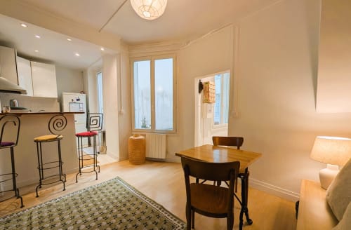 Spacious Paris apartment living area with dining table, kitchen bar seating, and windows overlooking Faubourg Saint-Denis