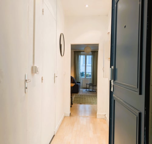 Modern hallway in Parisian apartment with white walls, wooden flooring, and view into bright living room with windows