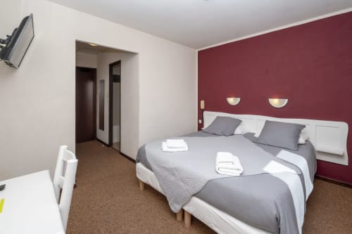 Chambre moderne de l'Hôtel Le Verdon avec lits jumeaux, mur d'accent bordeaux et éclairage avec vue sur le lac