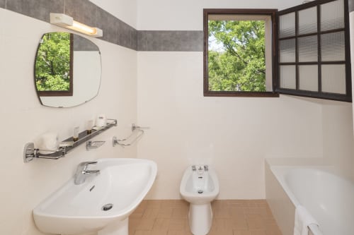 Salle de bains moderne à l'Hôtel Le Verdon avec lavabo, bidet, baignoire, miroir et fenêtre vue sur le village