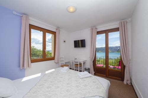 Chambre lumineuse à l'Hôtel Restaurant Le Verdon avec vue lac, portes en bois ouvrant sur balcon surplombant le lac de Verdon
