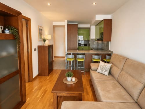 Moderno apartamento de planta abierta en Baiona con salón, cocina de muebles verdes, mobiliario de madera y sofá beige