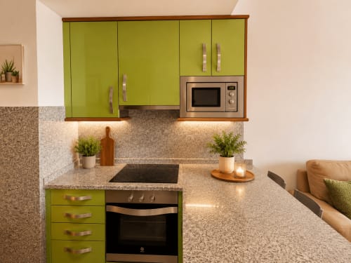 Cocina moderna con armarios verde lima, encimera de granito, microondas integrado y estufa de acero inoxidable en Baiona
