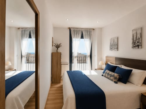 Dormitorio moderno con acentos azules, dos camas, vistas al balcón y muebles contemporáneos en apartamento Holibai, Baiona