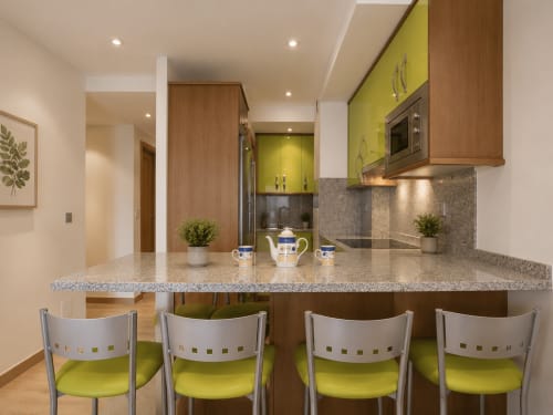 Cocina moderna con muebles verde lima, encimera de granito y cuatro sillas verde lima en la barra de la isla en Baiona
