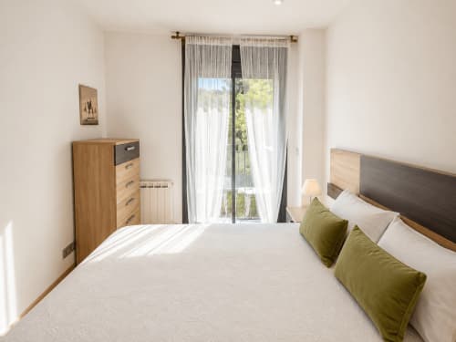 Luminosa habitación con cama matrimonial, almohadas verdes, muebles de madera y balcón con vistas a la piscina del apartamento Holibai en Baiona