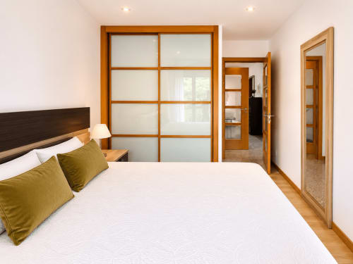 Dormitorio moderno en apartamento Afouteza, Baiona con cama matrimonial, almohadas oliva, muebles de madera y puertas de armario correderas