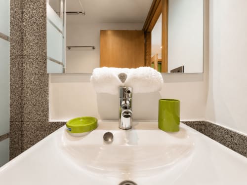 Lavabo moderno con toallas blancas, accesorios verdes y encimeras de granito en el apartamento Holibai de Baiona