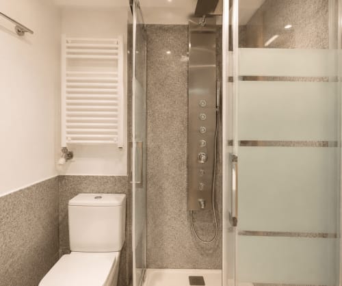 Baño moderno en apartamento Holibai, Baiona con ducha abierta, inodoro, toallero calefactor y azulejos de granito