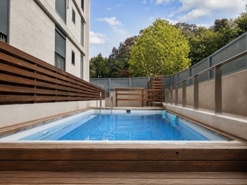 Piscina moderna en Holibai, Baiona, con terraza de madera, valla de privacidad metálica y vistas al bosque