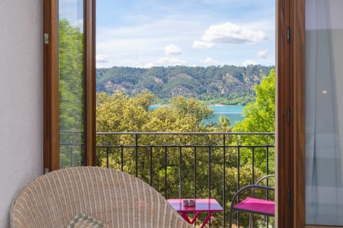 Balcon avec vue sur le lac à l'Hôtel Restaurant Le Verdon, portes ouvertes sur le lac de Verdon et les collines boisées