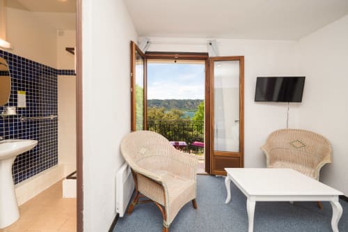 Chambre avec vue sur le lac au Hôtel Le Verdon, fauteuils en osier, table blanche et balcon panoramique sur Les Salles sur Verdon