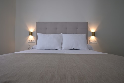 Habitación moderna del Hotel Boutique Alcazaba con cabecero tapizado en gris, almohadas blancas y apliques de latón