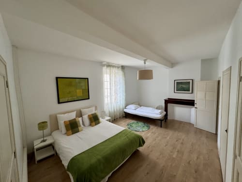 Chambre spacieuse du gîte de Verniolle avec lit double, lit simple, touches de vert, parquet et fenêtres sur jardin