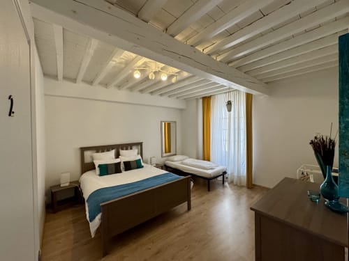 Chambre spacieuse du cottage de Verniolle avec poutres apparentes, lit queen-size, petit lit gigogne et vue sur le jardin par les fenêtres