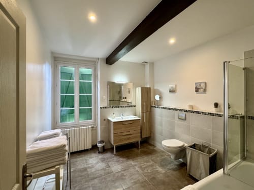 Salle de bain moderne du gîte Verniolle avec meuble en bois, carrelage foncé, douche et vue sur le jardin