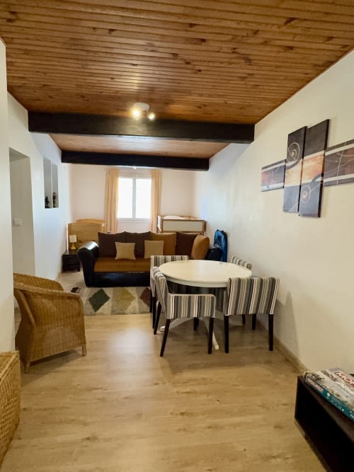 Séjour ouvert à la Gîte du Mercadal à Verniolle avec table à manger, canapé, fauteuils en rotin et poutres en bois apparentes.
