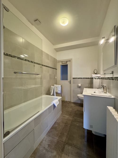 Salle de bain moderne du Gîte du Mercadal à Verniolle avec douche à l'italienne, meuble vasque blanc, carrelage mural et sol foncé.