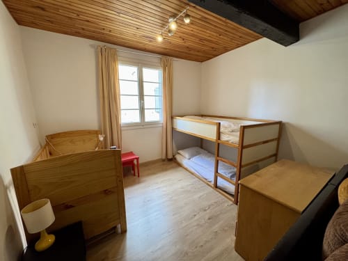 Chambre lumineuse du gîte avec plafond en bois, lit superposé, lit simple et vue sur le jardin au Gîte du Mercadal à Verniolle