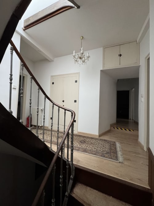 Palier d'escalier avec rampe en bois foncé, lustre, portes crème et parquet au gîte du Mercadal