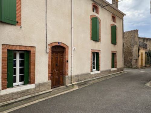 Charmant gîte villageois aux Pujols, Ariège, façade en pierre beige, volets verts et portes cintrées en brique