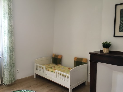 Chambre d'enfant avec lit blanc au Gîte du Cœur du Village à Verniolle, Ariège. Parure verte, meubles sombres.
