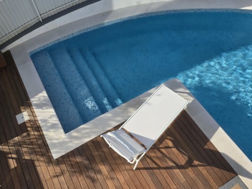 Espreguiçadeira branca em deck de madeira com vista para a piscina privada azul cintilante na villa Casa Cliff, Sesimbra