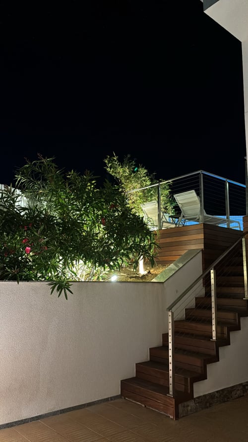 Vista noturna da escada de madeira e terraço da villa Casa Cliff em Sesimbra com piscina iluminada e plantas do jardim