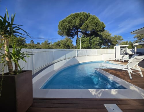 Piscina contemporânea com corrimãos brancos, espreguiçadeiras e exuberante vegetação mediterrânea na villa Casa Cliff, Sesimbra
