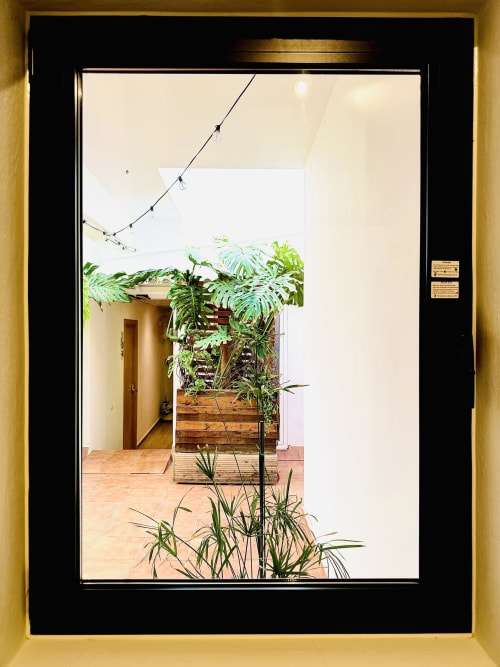 Veduta attraverso porta in vetro con cornice nera verso il patio lussureggiante di Nanit Rooms Ibiza, con fioriere in legno e terracotta
