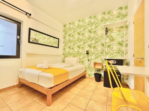 Helder eenpersoonskamertje in Nanit Rooms Ibiza met gele accenten, groen bladbehang, houten bed en tegelvloer