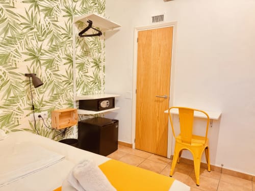 Camera moderna a Nanit Rooms Ibiza con carta da parati tropicale, sedia gialla, scrivania nera e porta in legno