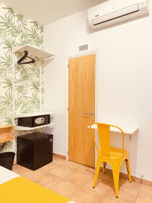 Camera luminosa a Nanit Rooms Ibiza con sedia gialla, porta in legno, carta da parati botanica verde e unità AC