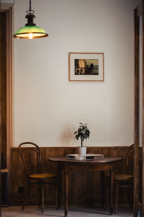 Coin repas intime au Savoy Hôtel avec table en bois, chaises en bois courbé, lampe suspendue et œuvre encadrée.