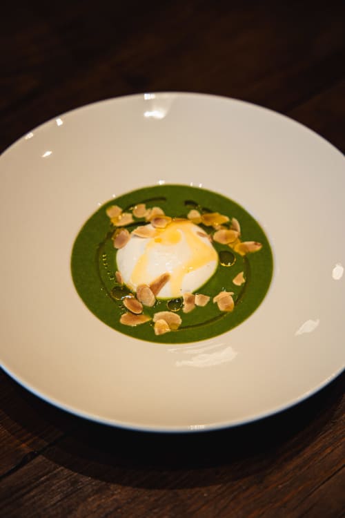Plat élégamment dressé au Savoy Hôtel : cœur crémeux blanc sur coulis vert vibrant garni de fruits secs, Le Bourget-du-Lac