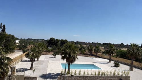 B&B Hélios hotel pool and courtyard with palm trees in Nardò, Italy, featuring bright blue swimming pool and white paved