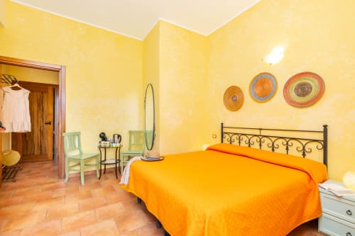 Bright yellow bedroom with orange bed at Agriturismo Chiai Francesco in Bari Sardo, Italy. Mediterranean-style decor with