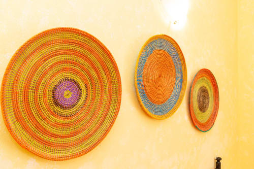 Three colorful woven circular placemats on yellow wall at Agriturismo Chiai Francesco in Bari Sardo