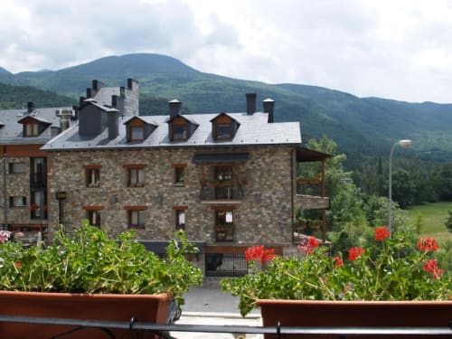 Hotel Llibrada en Benasque con fachada de piedra, vistas a las montañas y flores rojas en primer plano