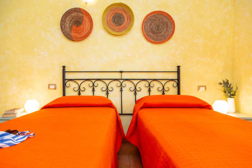 Bright bedroom at Agriturismo Chiai Francesco with two orange beds, black iron headboard, yellow walls, and colorful basket