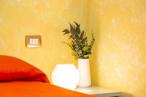 Bright yellow bedroom corner at Agriturismo Chiai Francesco with red bedding, white lamp, and dried flowers vase
