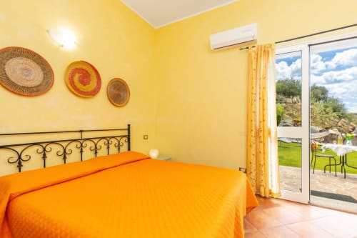 Bright yellow bedroom with orange bedding at Agriturismo Chiai Francesco in Bari Sardo, overlooking countryside
