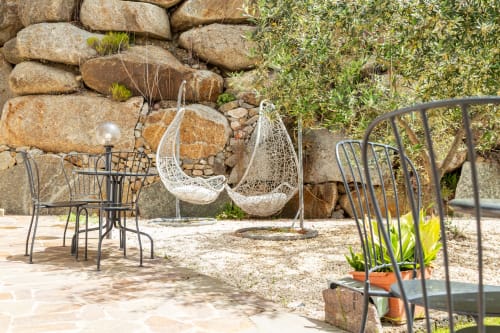 Rustic outdoor seating area at Agriturismo Chiai Francesco with hanging chairs, metal furniture, and stone wall backdrop in